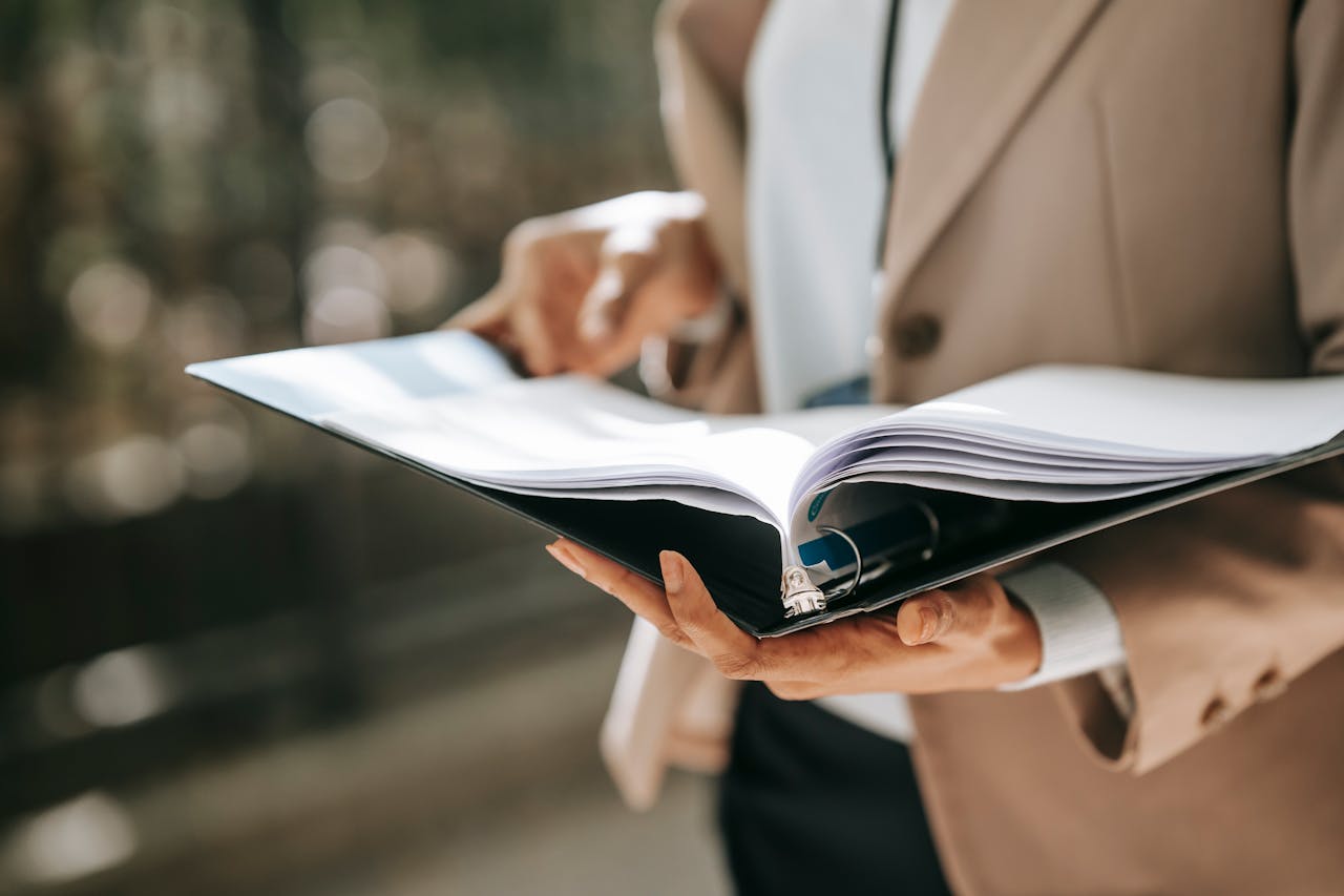 Crop faceless female entrepreneur in formal jacket turning pages of documents in folder while reading